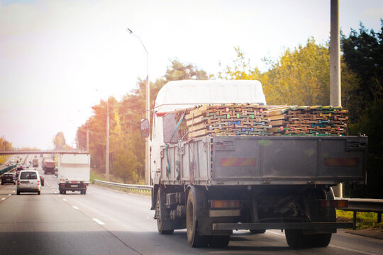 Heavy truck transports construction material on highway. Cargo bed loaded with wooden planks and scaffolding elements. Sunny day road transport.