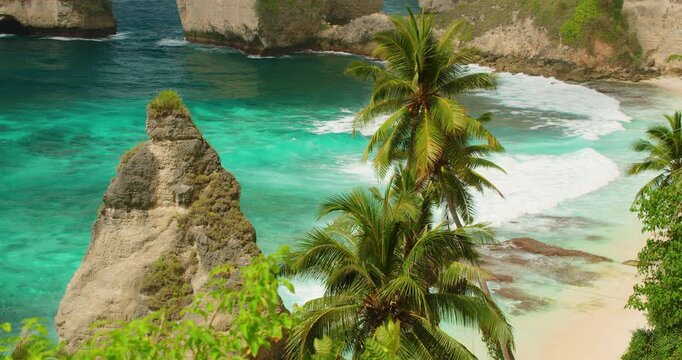 Palm trees overlook crashing ocean waves and turquoise water at Diamond Beach Bali
