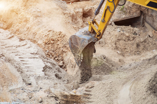 Close up view of excavator bucket moving sand and soil on construction site, heavy machinery performing earthwork operations, sunlight illuminating digging activity, industrial equipment in action