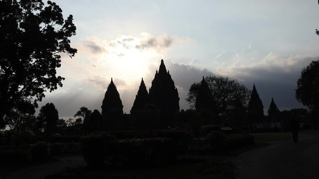 Silhouetted temple peaks reach toward a radiant sky. Sunlight spills through clouds, casting sacred rays. Ancient architecture stands still against a quiet horizon. Mystical glow suggests reverence
