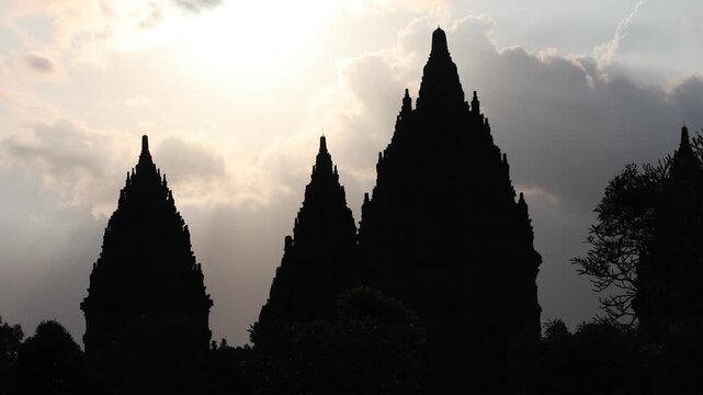 Silhouetted temple peaks reach toward a radiant sky. Sunlight spills through clouds, casting sacred rays. Ancient architecture stands still against a quiet horizon. Mystical glow suggests reverence