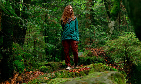 Woman in hiking gear pauses on a mossy forest path surrounded by lush greenery verdant woodland, taking in the serene natural environment