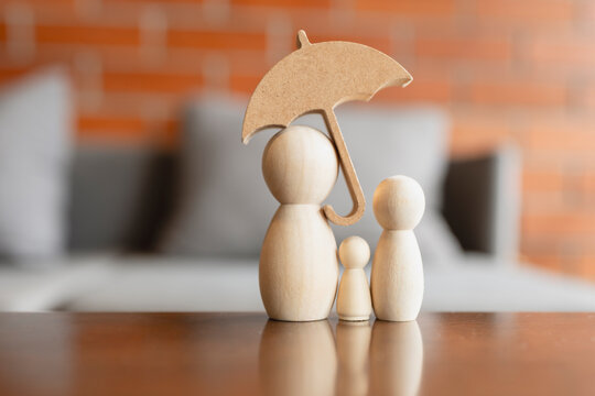 Holistic family healthcare and life insurance concept with wooden peg doll figures sheltered under umbrella on table for child education fund, domestic protection and welfare security.