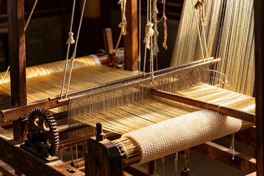 Traditional wooden loom in operation, weaving fabric with threads and mechanical components