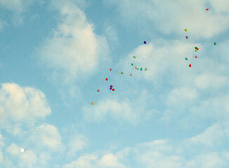 Small colorful balloons drifting across a cloudy blue sky © Bogdan_V