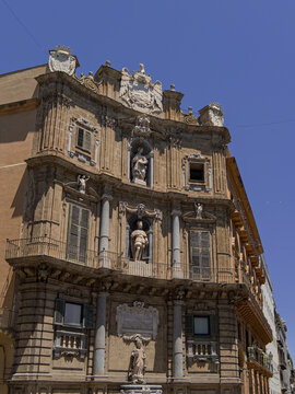 Eye-level architectural photograph of the concave Baroque facade at Quattro Canti in Palermo, Sicily, detailing the historic statues of Summer, King Philip II, and Saint Ninfa under a bright blue sky.