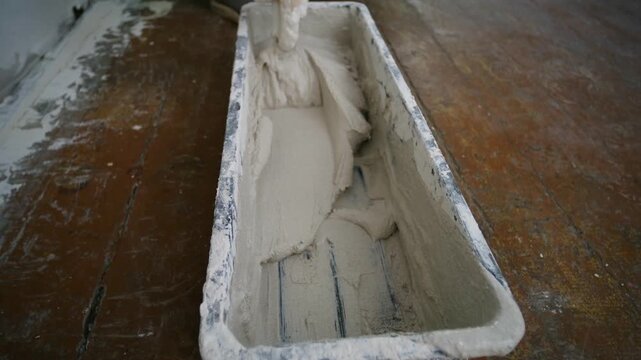 Professional worker hand mixing finishing plaster compound putty knife in plastic trough, preparing material for drywall repairs, home renovation on wooden floor. Worker mixing plaster putty in trough