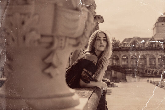 Beautiful blonde woman in gothic dress posing in vintage sepia photo style with scratched texture near classic baroque architecture 