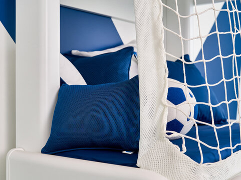 Soccer themed bedroom with a football and pillows. The bed is white with blue accents and a white net, reminiscent of a soccer goal