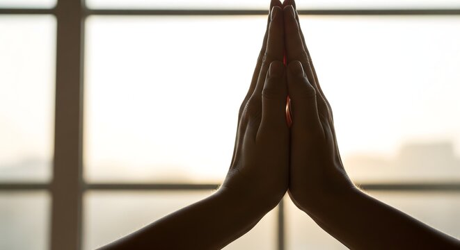 Silhouette of hands pressed together in a prayer position against light