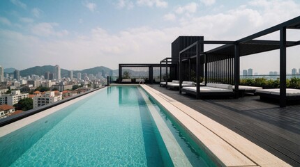 Obraz premium Rooftop infinity pool overlooks cityscape. Modern lounge beds offer relaxation by turquoise water. Buildings and hills form background skyline on sunny day. Luxury urban resort destination.