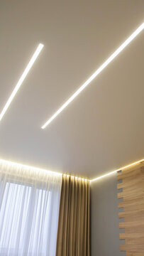 Modern apartment room interior design showcasing minimalist ceiling lighting solution, two linear LED strips providing bright illumination, contemporary home decor vertical photo