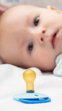 Infant baby with curious open eyes, pacifier in foreground on white blanket, serene childhood development, innocence of new life, vertical photo