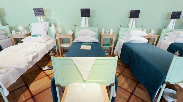 Numbered beds stand in a row inside the hospital ward of the Lyceum in Pushkin, Saint Petersburg. The neat historical room evokes a quiet feeling of nostalgic care.