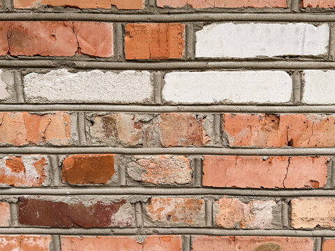Close-up of weathered brick wall with mixed red and white bricks, textured masonry surface with visible mortar and cracks