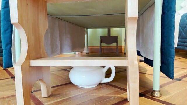 A white chamber pot sits under a wooden bench on parquet floor in Pushkin, Saint Petersburg. This simple detail evokes a humble and nostalgic feeling.