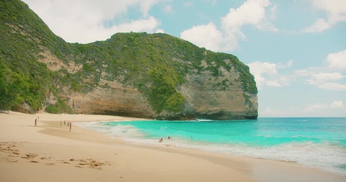 Dramatic cliff towers over sandy beach with blue ocean water in Bali Nusa Penida