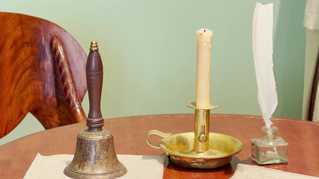 A brass bell and candle rest on a wooden table inside the historic Lyceum in Pushkin, Saint Petersburg. The intimate setting inspires a quiet feeling of nostalgic wonder.