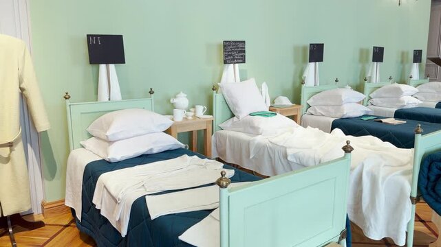 Single beds stand neatly in an infirmary ward at the Imperial Lyceum in Pushkin, Saint Petersburg. Soft light fills the quiet room. This orderly display evokes a peaceful and nostalgic feeling.