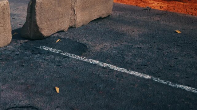Rocks block part of a black asphalt road which has a white line painted on it. Leaves are scattered on the surface under natural light during daytime.