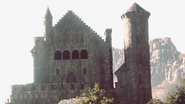 A large stone castle is located near mountains. The sun shines brightly, highlighting the sturdy walls and towers of the structure. Trees surround the area, adding greenery.