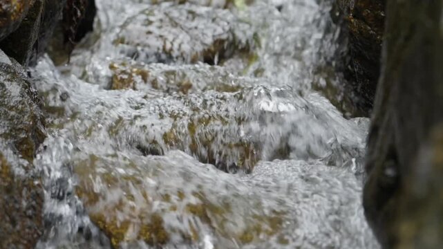 Closeup of fast flowing water over stones in narrow canal