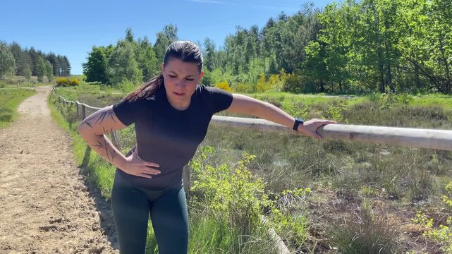 A woman jogging outdoors in nature is experiencing pain and a stitch	
