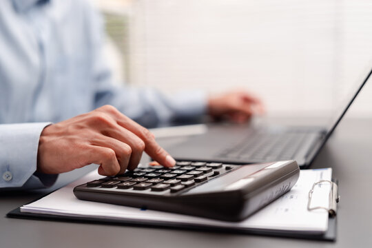 Business finance accounting budget and data analysis. Man hand pressing calculator on clipboard document near laptop computer on desk.