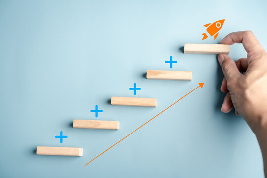 Business growth startup launch and success strategy. Hand placing wood block step on stairs with rocket icon and upward arrow.