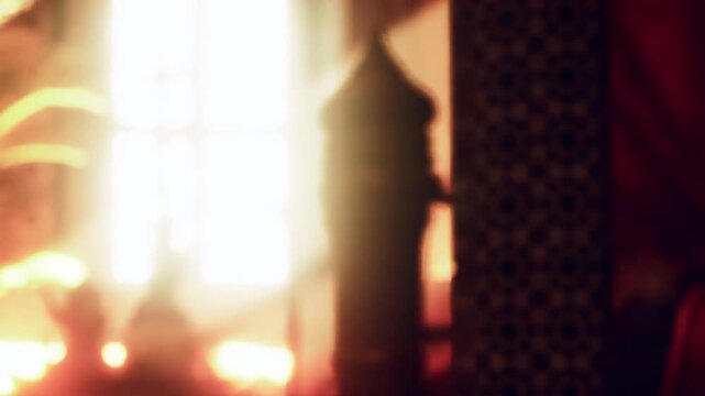 Bright light enters through a window and creates a warm atmosphere in the room. Decorative patterns on the wall and curtains add to the setting. The space seems inviting and cozy.
