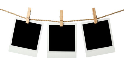 Three blank instant photo prints hanging on a rope with wooden clothespins, isolated on transparent background © STUDIOP