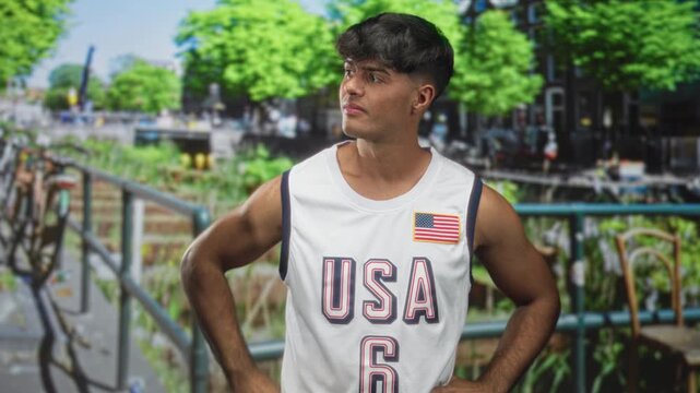 Man in usa basketball jersey scratches head showing bare arm on a street railing; pensive uncertainty.