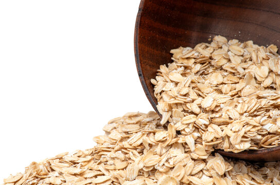 Oats spilling from wooden bowl with white background and copy space.