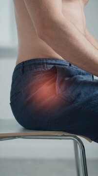 Man sitting on a chair with red glowing highlight on his hip representing joint pain, inflammation, or sciatica discomfort