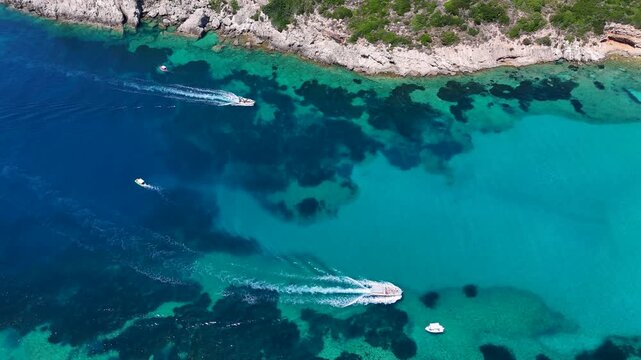 Aerial view of Porto Timoni beach with small boats moving through the turquoise waters of the Ionian Sea in Kerkira, Greece.