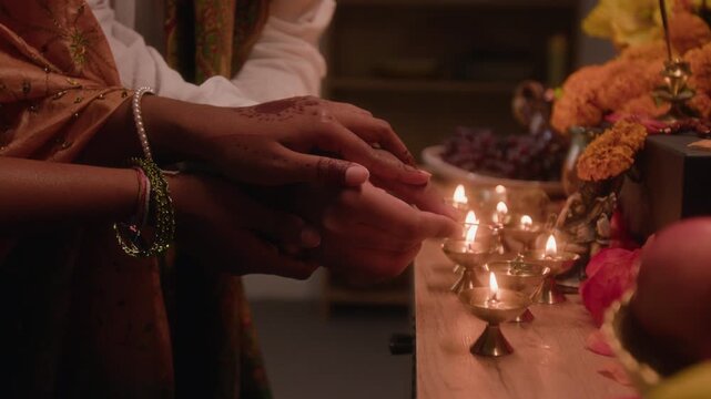 Tilt up shot of young Indian couple lighting traditional brass oil lamps during Diwali festival celebration. Video serves holiday marketing campaigns and cultural projects