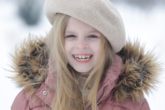 Outdoor winter portrait of adorable 8 year old girl wearing beige woolen beret and pink winter jacket with fur detail