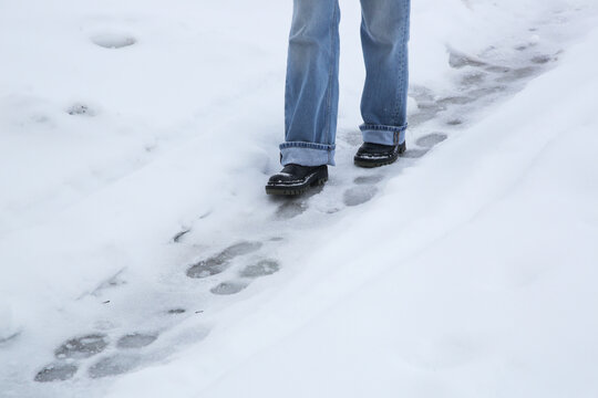 Danger of slipping. Person in chunky platform leather boots walking on snowy icey road