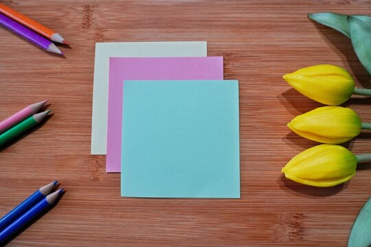 Blank colorful sticky notes with colored pencils and yellow tulips on wooden background