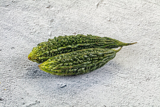 Two fresh green bitter melons with bumpy texture on light gray textured surface, natural lighting, shallow depth of field