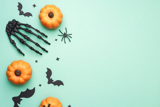 Orange pumpkins bats skeleton hand spider on mint background festive Halloween decor.