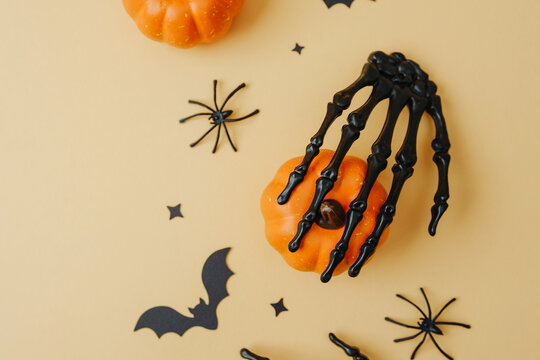 Skeleton hand grasps small pumpkin surrounded by black bats and spiders on orange background