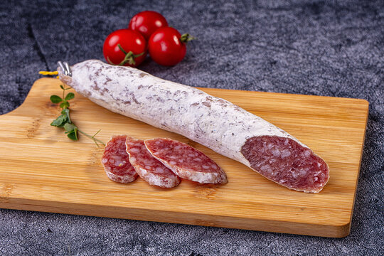 Fuet sausage on wooden cutting board with sliced pieces and cherry tomatoes, rustic food presentation
