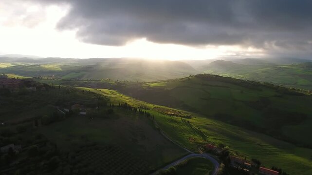 Aerial view of rolling hills of Tuscany at sunset with dramatic sun rays illuminating the green landscape in Tuscany, Italy.