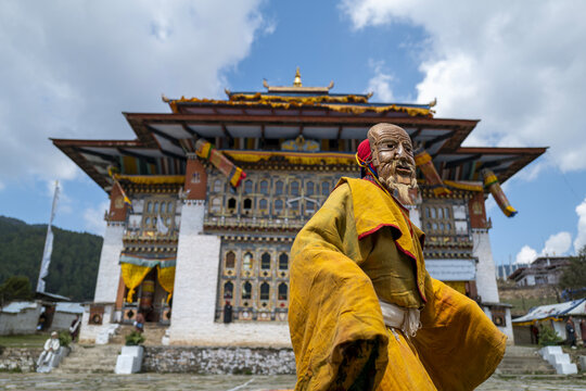 Masked cham dancer in a yellow robe in front of a dzong gate, Thimphu District, Thimphu, Bhutan
