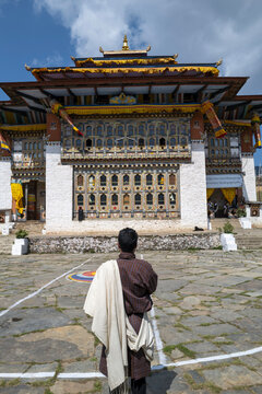 Man in traditional gho facing a decorated monastery building, Thimphu District, Thimphu, Bhutan