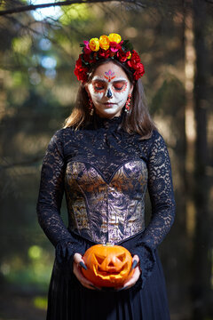 Young woman with closed eyes in forest with Halloween pumpkin in hand. Santa Muerte makeup.