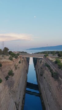 Vertical aerial drone above Isthmus of Corinth at sunset, Greece. Bridges and crossing traffic visible. Clear day, few clouds. Golden light on canal