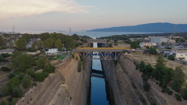 Aerial drone shot above Isthmus of Corinth at sunset. Bridges and crossing traffic visible. Clear day, few clouds. Golden evening light