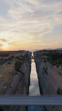Corinth Canal, Greece. Vertical aerial drone at sunset. Bridges span canal, cars crossing. Clear day, few clouds. Dramatic golden light